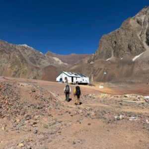 Trekker walking towards high-altitude camp on Aconcagua surrounded by rugged terrain