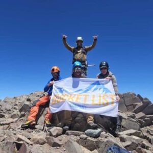 Mountaineers holding The Bucket List Company flag on Aconcagua summit