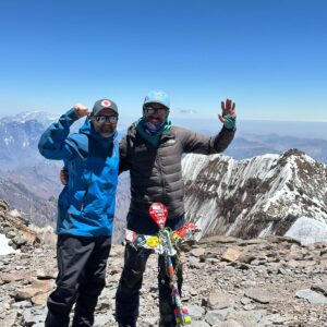 Two climbers celebrating on the summit of Mount Aconcagua with snowy peaks behind