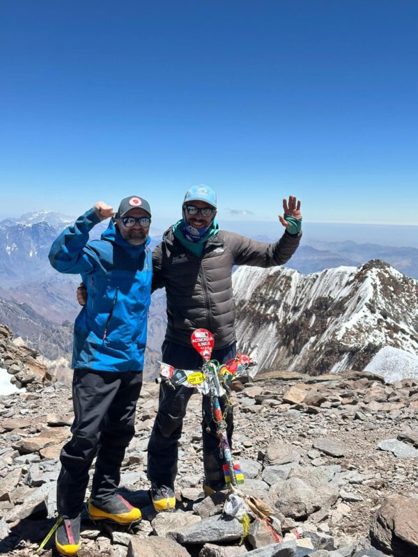 Two climbers celebrating on the summit of Mount Aconcagua with snowy peaks behind