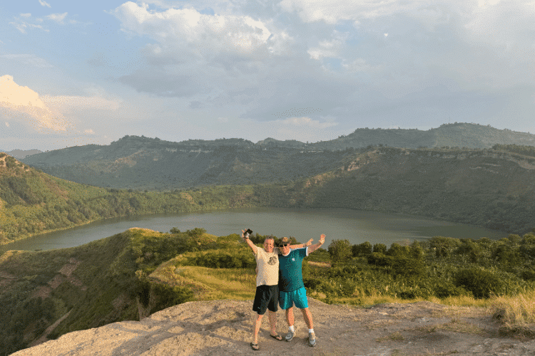 Travellers standing on a viewpoint overlooking a crater lake landscape in Uganda.