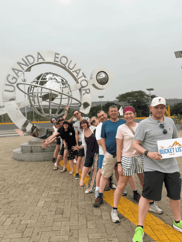 Group of travellers standing at the Uganda Equator monument during a guided tour.