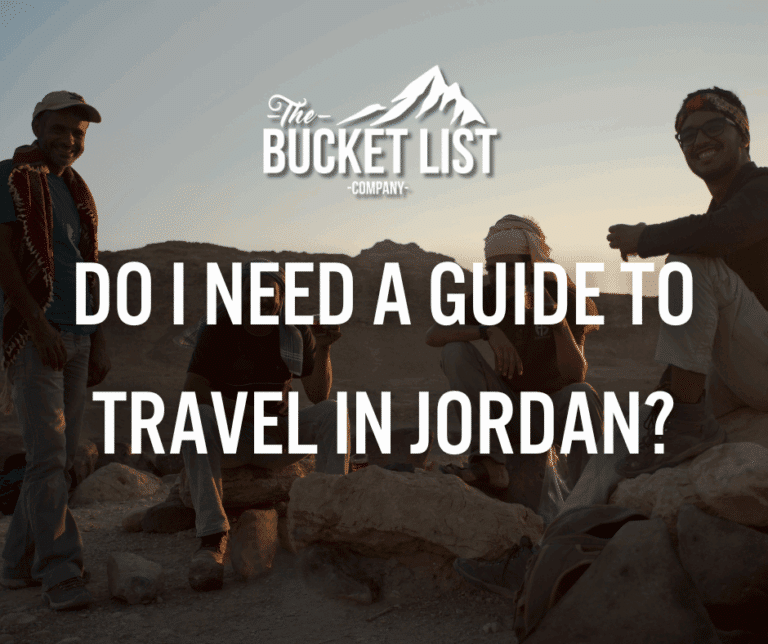 Four travelers sit on rocky terrain at sunset smiling and relaxing Overlaid text reads “Do I need a guide to travel in Jordan?” with "The Bucket List Company" logo featuring a mountain above