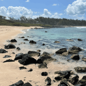 Quiet sandy beach in Mauritius with rocky shoreline and clear blue water.