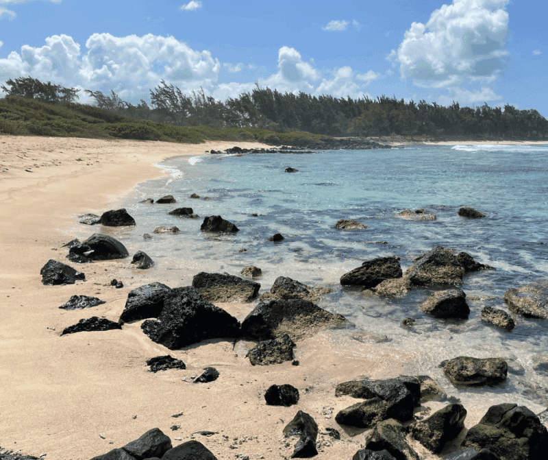 Quiet sandy beach in Mauritius with rocky shoreline and clear blue water.