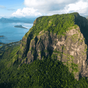 Aerial view of a dramatic mountain ridge in Mauritius surrounded by lush green forest and coastline.