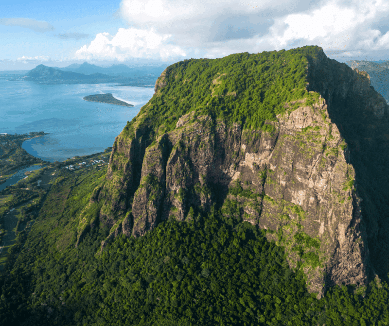 Aerial view of a dramatic mountain ridge in Mauritius surrounded by lush green forest and coastline.