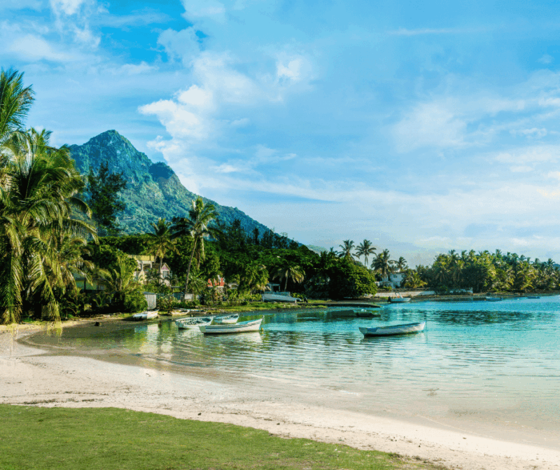 Calm lagoon in Mauritius with small boats anchored near a palm-lined beach and mountain backdrop.