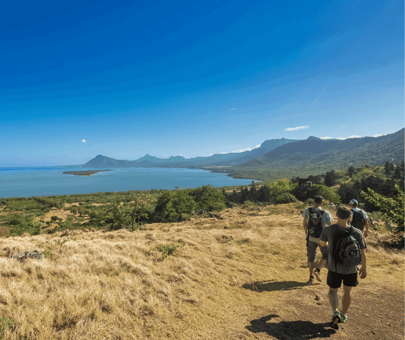 Group hiking along a hillside trail in Mauritius with panoramic views over the lagoon and mountains.
