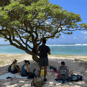 Group resting in the shade on a sandy beach in Mauritius with turquoise ocean in the background.