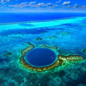 Aerial view of the Great Blue Hole a large circular marine sinkhole surrounded by vibrant turquoise waters and coral reefs under a bright blue sky with scattered clouds